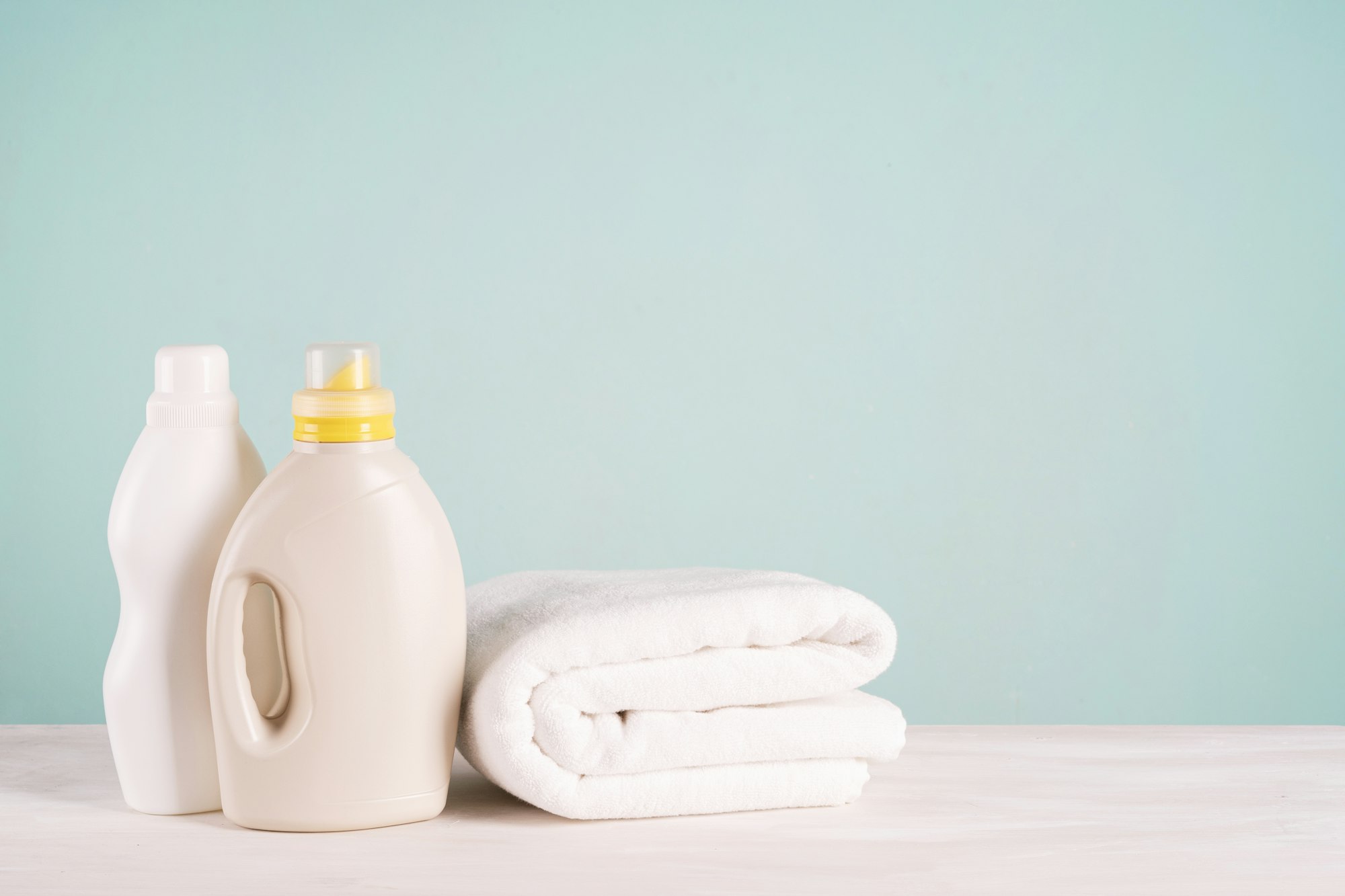 A bottle of laundry detergent, fabric softener and a stack of clean laundry on a blue background.