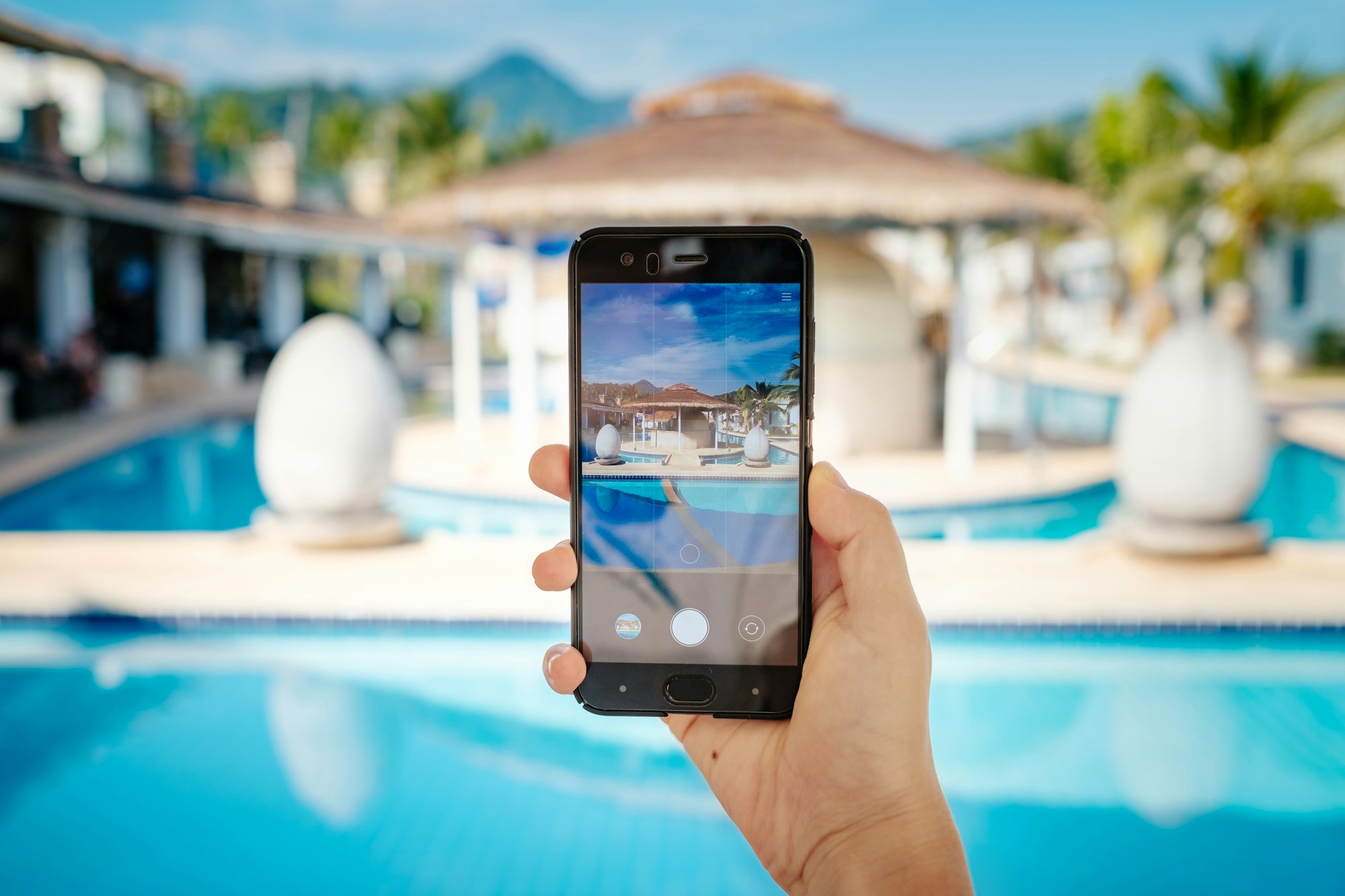 hand holding phone on background of the pool in hotel. photo camera on the screen.