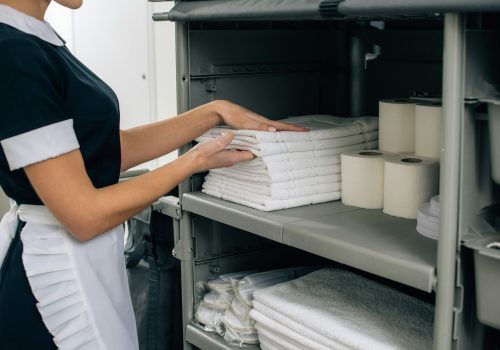 cropped shot of maid in uniform taking towels from shelf of housekeeping cart